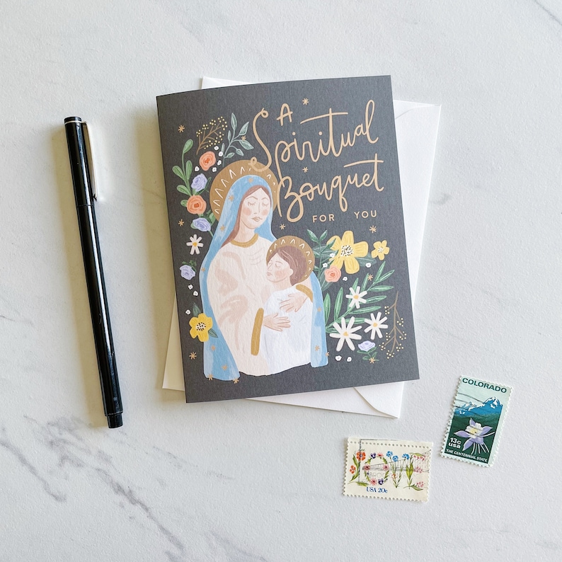 May include: A greeting card with a dark gray background featuring a colorful illustration of Mary and baby Jesus surrounded by flowers. The text on the card reads "A Spiritual Bouquet For You".