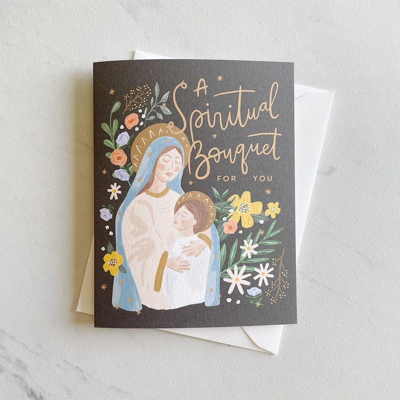 May include: A black card with a gold inscription that reads "A Spiritual Bouquet For You". The card features a colorful illustration of Mary and Jesus surrounded by flowers.