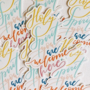 K&ouml;nnte beinhalten: Eine Sammlung bunter Aufkleber mit dem Spruch "Holy Spirit you are welcome here", geschrieben in verschiedenen Schriftarten und Farben. Die Aufkleber befinden sich auf einem wei&szlig;en Hintergrund.