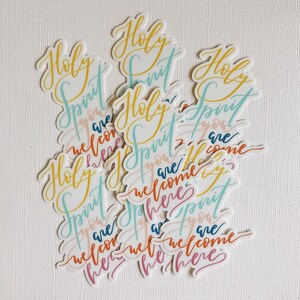 K&ouml;nnte beinhalten: Ein Stapel bunter Aufkleber mit den Worten "Holy Spirit you are welcome here", die in Handschrift geschrieben sind.