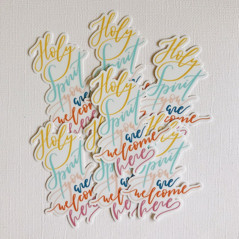 K&ouml;nnte beinhalten: Ein Stapel bunter Aufkleber mit den Worten "Holy Spirit you are welcome here", die in Handschrift geschrieben sind.