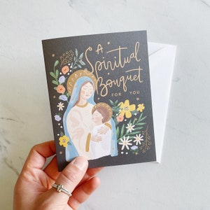 May include: A black card with a floral design and a painting of Mary and Jesus. The text on the card reads "A Spiritual Bouquet For You".