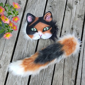 May include: A calico cat costume set with a black, orange, and white fur tail and a matching face mask with green eyes.