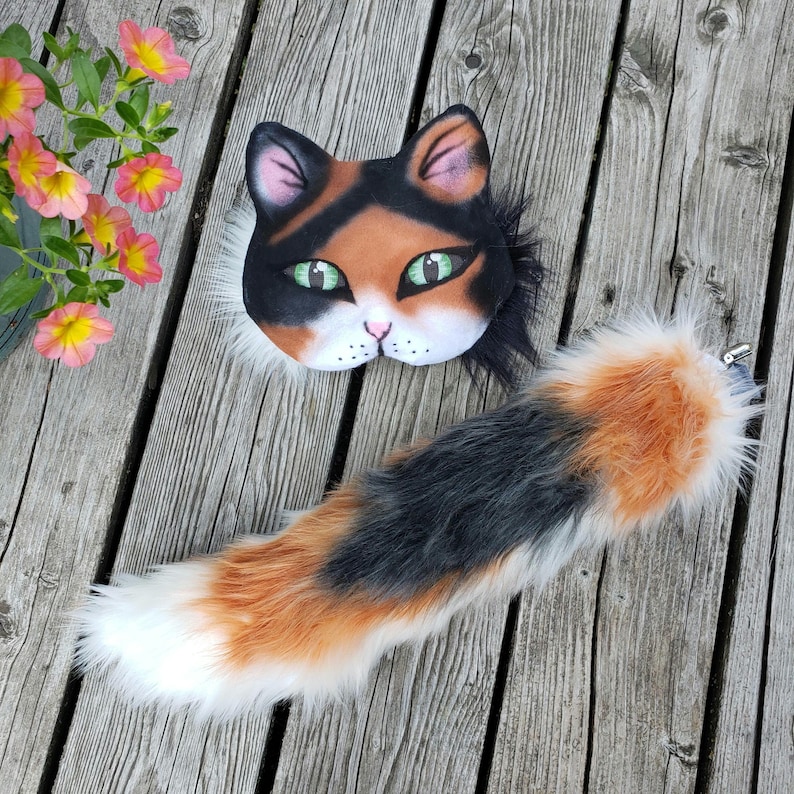May include: A calico cat costume set with a black, orange, and white fur tail and a matching face mask with green eyes.