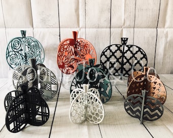 May include: A collection of decorative laser-cut pumpkin decorations in various colors and patterns. The pumpkins feature intricate designs, including floral, geometric, and plaid patterns. The color palette includes orange, black, white, and green, perfect for fall decor.