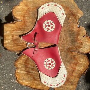 May include: A pair of red leather cowboy boot tops with white fringe and a star-shaped design. The boot tops have a red jewel in the center of the star.