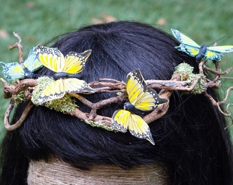 May include: A twig crown with yellow and blue butterflies attached. The crown is made of natural branches and has a mossy base.