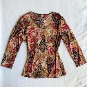 May include: A long-sleeve shirt featuring a complex pattern of black, red, and tan paisley and floral motifs. The garment has a rounded neckline and a fitted silhouette, with the intricate design covering the entire front and the sleeves.