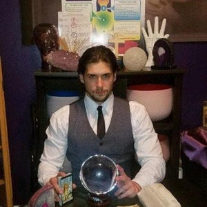 Psychic reader Derrek channeling intuitive guidance over a spread of tarot cards and glowing crystals for a fast same-day written report in PDF format.