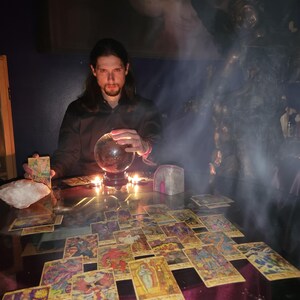 Spiritual counselor Psychic Derek reading tarot cards at a sacred table featuring a detailed white angel statue, healing crystals, and flickering candles.