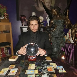 Psychic Derek conducting an online psychic reading beside a serene angelic figurine, natural gemstone crystals, a crystal ball, and burning incense smoke.