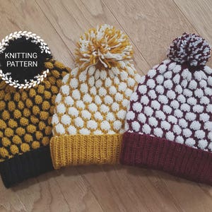 May include: Three knitted beanies with a textured dot pattern and pom-poms. One beanie is mustard yellow with a black brim, another is yellow with a white dot pattern and brim, and the third is burgundy with a white dot pattern and brim. The text "KNITTING PATTERN" is in a circle.