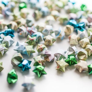 May include: A collection of origami stars made from paper maps in shades of green, blue, and white. The stars are scattered on a white surface.