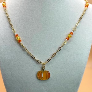 以下が含まれることがあります： オレンジと黄色のガラスビーズと小さなカボチャのチャームが付いたゴールドチェーンネックレスです。