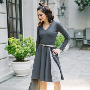 May include: A woman wearing a gray dress with a white and gray patterned skirt, a brown belt, and yellow heels. She is standing in front of a building.