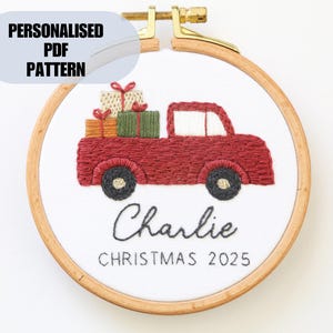 Puede incluir: Arte de aro navideño bordado con un camión rojo que transporta regalos. El diseño incluye el nombre "Charlie" y el año "2025". El texto "Personalised PDF Pattern" está en la parte superior. El bordado está en un aro de madera.