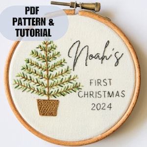 Pode incluir: Ornamento de Natal bordado com uma árvore verde, um vaso castanho e o texto "Noah's First Christmas 2024".