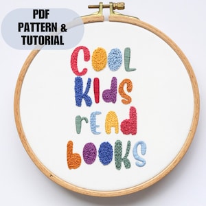 May include: Embroidered hoop art with the phrase "Cool Kids Read Books" in colorful, puffy letters. The letters are stitched in a variety of colors, including red, orange, yellow, green, blue, and purple.