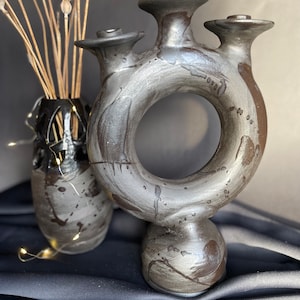 May include: A black ceramic candle holder with a ring design and three candle holders. The holder has a speckled and streaked glaze.