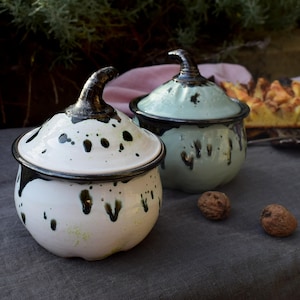 Peut inclure: Deux pots en céramique en forme de citrouille avec un couvercle, à glaçure mouchetée noire et blanche. Le pot de gauche est blanc avec des mouchetures noires, et le pot de droite est bleu clair avec des mouchetures noires.