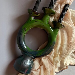 May include: A green ceramic candle holder with three arms, each holding a black textured candle. The holder has a circular design with a base. The piece is glazed in shades of green and black.