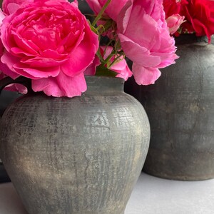 Peut inclure: Deux pots en céramique gris foncé avec une surface rugueuse et texturée. Les pots sont remplis de roses roses et d'une seule rose rouge.