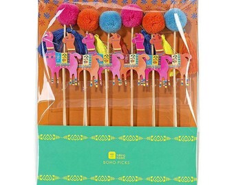 May include: A set of eight colorful llama cake toppers with pom poms. The toppers are made of cardboard and have a wooden stick attached to the back. The pom poms are in shades of pink, orange, and blue. The llamas are decorated with colorful patterns and have tassels hanging from their necks. The packaging says "boho picks".