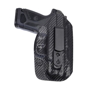 May include: A black carbon fiber holster with a black clip and a black handgun with the word "RUGER" printed on the side.