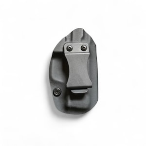 May include: A black, molded polymer holster with a metal belt clip. The holster has a curved shape and is secured with screws. The clip is centered on the holster and is designed to attach to a belt. The holster is designed to carry a firearm.