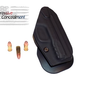 May include: Black holster with a metal clip and three bullets. The text "Aggressive Concealment" is displayed above the holster against a white background with a faded American flag.