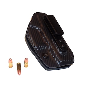 May include: A black leather holster with a carbon fiber pattern and a belt clip. Three copper-colored bullets are in the foreground.
