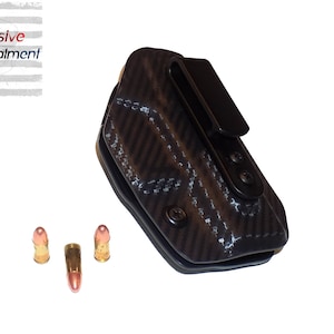 May include: A black carbon fiber pattern holster with a black clip and three bullets. The text "Aggressive Concealment" is in the upper left corner.