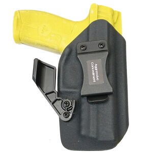 May include: A black holster with a clip and a yellow handgun inside. The holster has the text "Aggressive Concealment" on it.