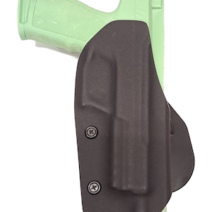 May include: A black plastic holster for a handgun with two visible screws. The holster is designed to be worn on the belt.