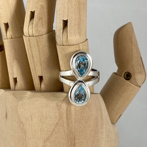 Può includere: Un anello d'argento con due pietre preziose di topazio blu a forma di goccia.