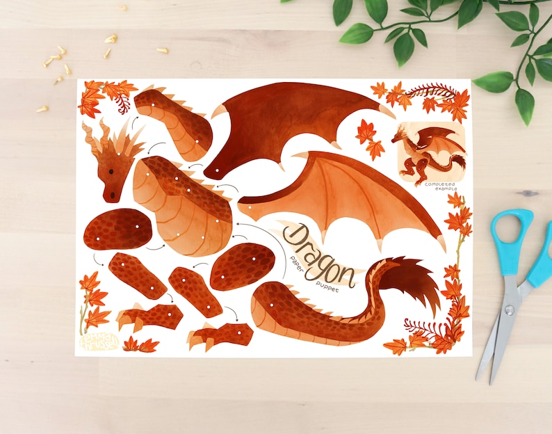 Puede incluir: Un kit de marioneta de drag&oacute;n de papel con varias piezas marrones y naranjas, incluyendo alas, cabeza y partes del cuerpo. Las palabras "Dragon paper puppet" est&aacute;n escritas en la imagen, junto con un ejemplo completo. Unas tijeras con mango azul est&aacute;n a la derecha.