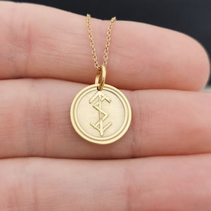 May include: A gold necklace with a round pendant featuring a symbol of three triangles. The pendant is on a delicate chain.