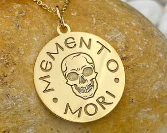 May include: Gold necklace with a round pendant featuring a skull and the text "Memento Mori".
