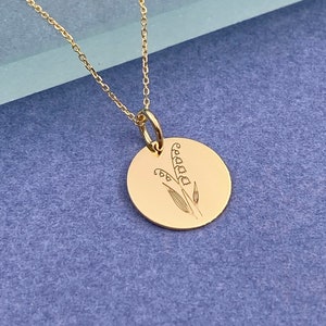 May include: A gold necklace with a round pendant featuring an engraved lily of the valley design.
