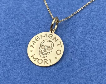 May include: A gold necklace with a round pendant featuring a skull and the words "Memento Mori".