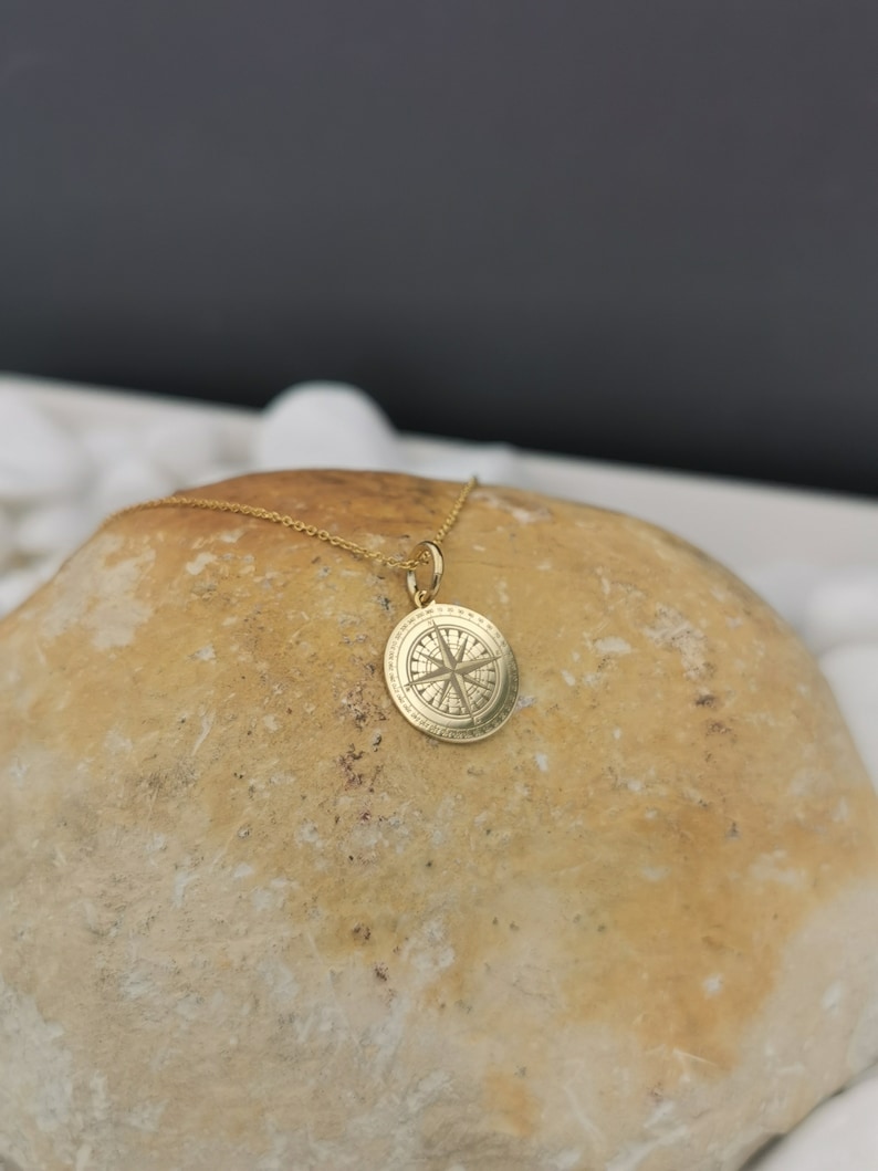 Compass engraved, circular,
solid gold pendant 14k,
the size is 0,5 iches / 12,7 millimeter.
Thickness 0,5 milimiters.
The hoop on top is circular and gold as well.
 The finish of the pendant in shinny.