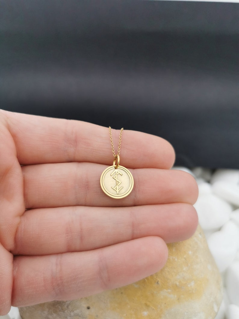 May include: A gold chain necklace with a round pendant featuring a Norse symbol. The pendant is about 1 inch in diameter.