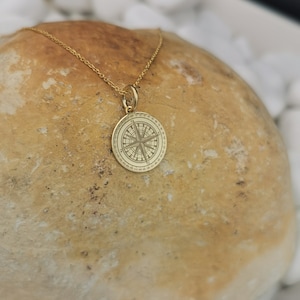 Compass engraved, circular,
solid gold pendant 14k,
the size is 0,5 iches / 12,7 millimeter.
Thickness 0,5 milimiters.
The hoop on top is circular and gold as well.
 The finish of the pendant in shinny.