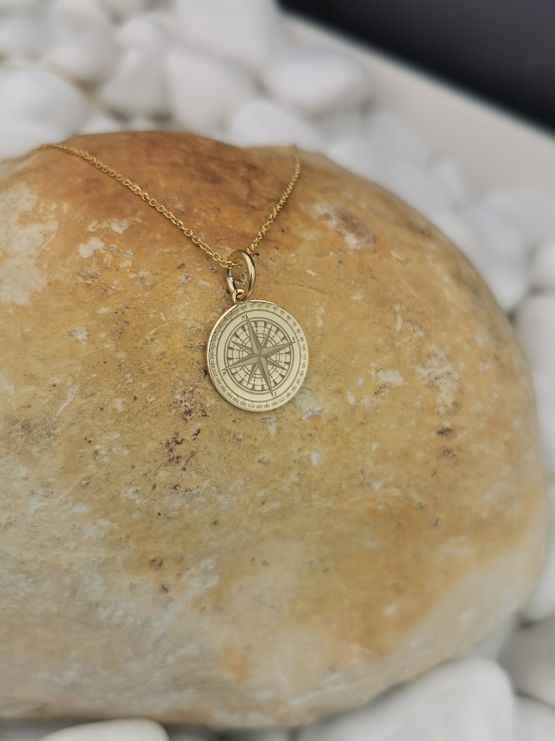 Compass engraved, circular,
solid gold pendant 14k,
the size is 0,5 iches / 12,7 millimeter.
Thickness 0,5 milimiters.
The hoop on top is circular and gold as well.
 The finish of the pendant in shinny.