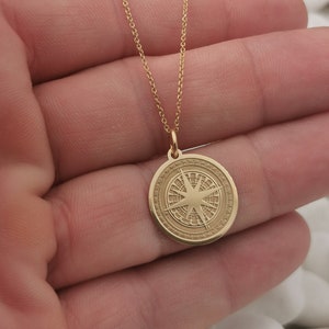 Compass engraved, circular,
solid gold pendant 14k,
the size is 0,75 iches / 19,1 millimeter.
Thickness 0,5 milimiters.
The hoop on top is circular and gold as well.
 The finish of the pendant in shinny.
