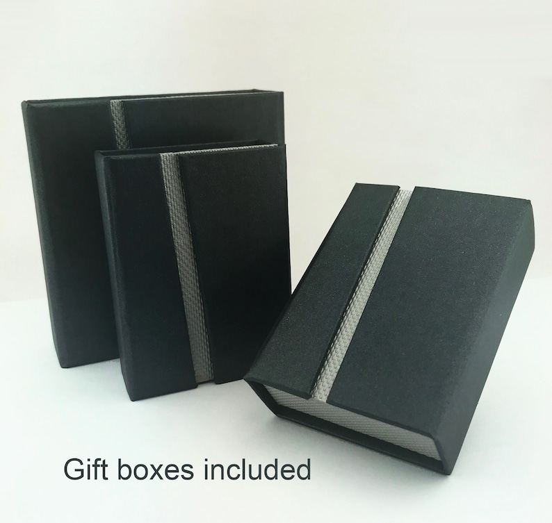 May include: Three black gift boxes with a silver stripe down the center. The boxes are nested inside each other, with the largest box at the back and the smallest box in the front. The text "Gift boxes included" is printed below the boxes.