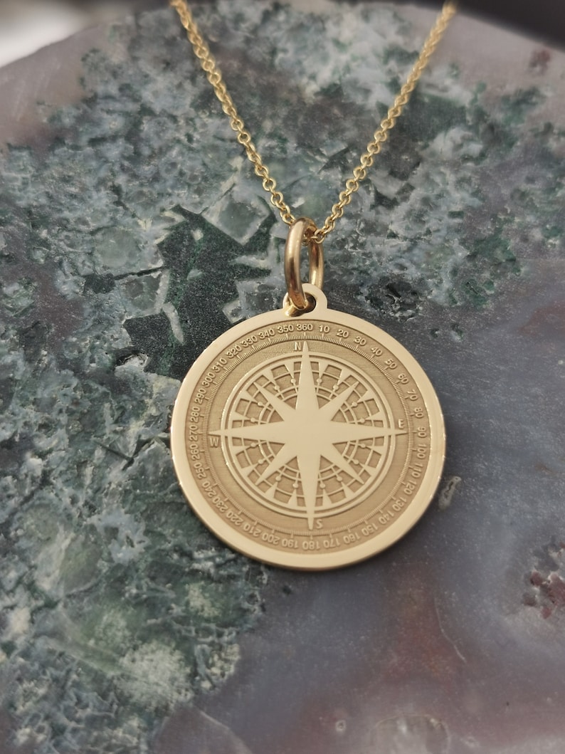 Compass engraved, circular,
solid gold pendant 14k,
the size is 0,75 iches / 19,1 millimeter.
Thickness 0,5 milimiters.
The hoop on top is circular and gold as well.
 The finish of the pendant in shinny.