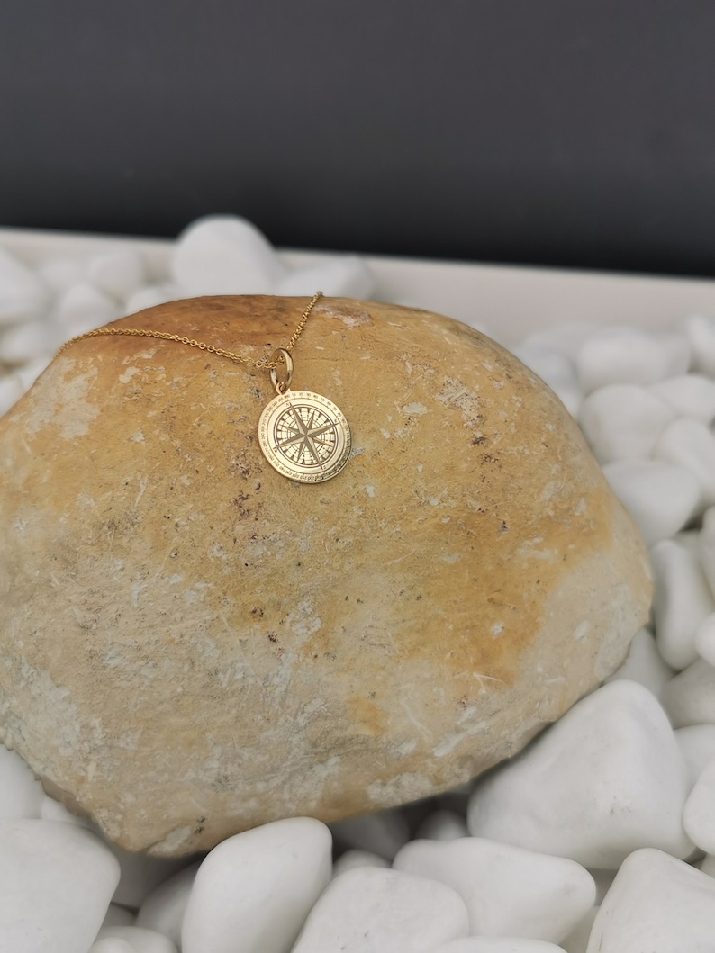 Compass engraved, circular,
solid gold pendant 14k,
the size is 0,5 iches / 12,7 millimeter.
Thickness 0,5 milimiters.
The hoop on top is circular and gold as well.
 The finish of the pendant in shinny.
