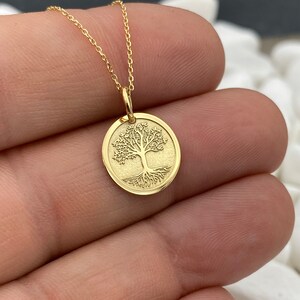 May include: A gold-colored necklace featuring a circular pendant with a detailed tree design. The tree has a full crown and visible roots. The pendant hangs from a delicate gold chain, creating an elegant and symbolic piece of jewelry.