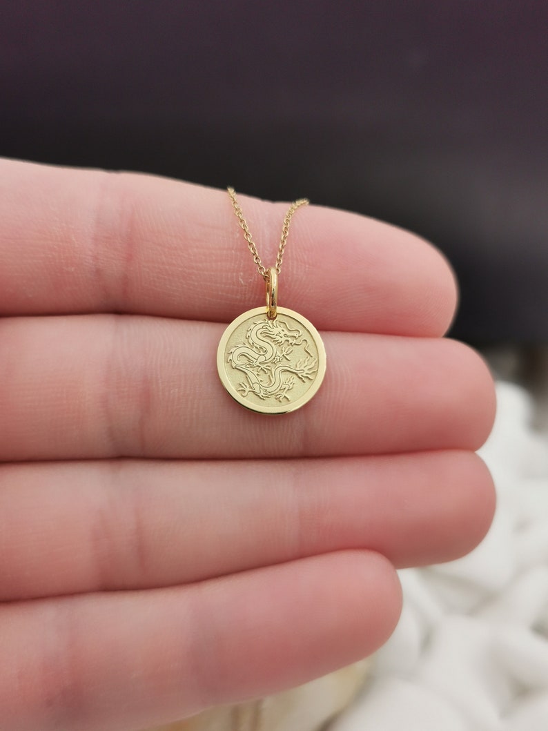 Chinese Dragon engraved, circular,
solid gold pendant 14k,
the size is 0,5 iches / 12,7 millimeter.
Thickness 0,5 milimiters.
The hoop on top is circular and gold as well.
 The finish of the pendant in shinny.